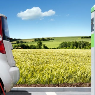 A small EV next to a charging station, yellow field in the background