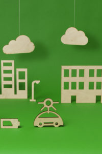 Wooden model of a green city with buildings, trees, an electric car and a charging point